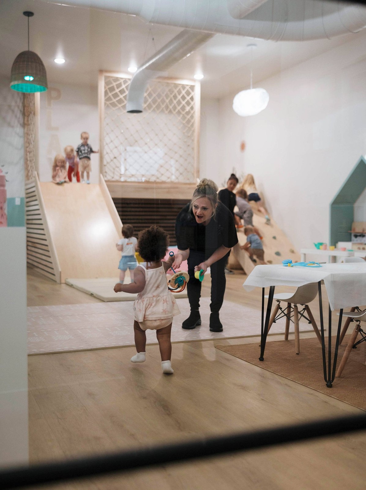 A Chasing Cali playspace staff member engaging with a toddler near the indoor slide and play area